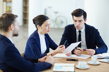 Group of business co-workers discussing paper held by woman