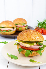 Burgers with sausage, cheese, tomato, arugula and soft bun with sesame seeds on a white wooden background. Vertical view