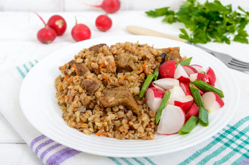 Buckwheat porridge with pieces of meat and a salad of radishes on a white wooden background.