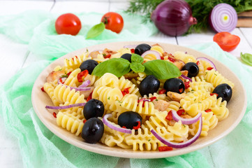 Pasta salad radiatori with chicken, black olives, blue onion, sweet pepper on a white wooden background.