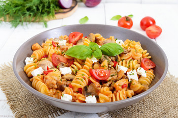 Pasta Radiatori with chicken, mushrooms, cherry tomatoes, feta cheese and tomato sauce on a white wooden background.