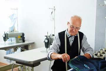 Portrait of old man working in tailoring studio making clothes and hand stitching cloth