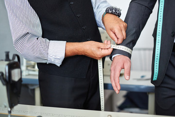 Closeup shot of old-fashioned tailor taking wrist measurements from client in small atelier studio to make custom classic suit with jacket