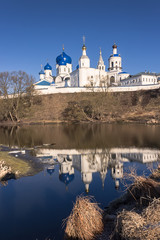 White-stone monastery with sky-blue domes, reflected in the edge of the last winter ice
