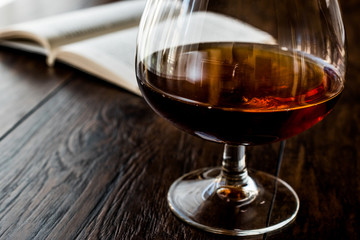 Glass of Cognac with a book on wooden surface.