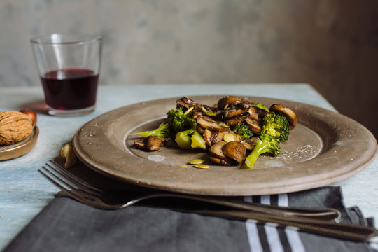 Saut&eacute;ed mushrooms with olive oil, broccoli and pumpkin seeds, on a concrete plate. At the table set