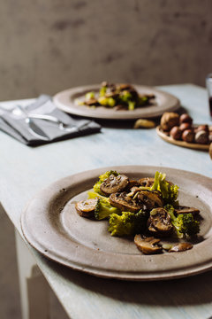 Saut&eacute;ed mushrooms with olive oil, broccoli and pumpkin seeds, on a concrete plate. At the table set