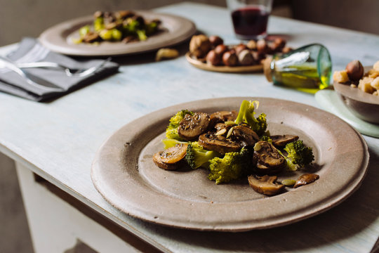 Saut&eacute;ed mushrooms with olive oil, broccoli and pumpkin seeds, on a concrete plate. At the table set