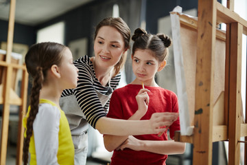 Two schoolgirls listening to teacher explanations while painting