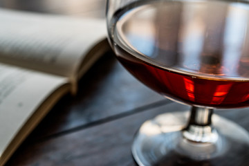 Glass of Cognac with a book on wooden surface.