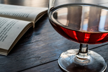 Glass of Cognac with a book on wooden surface.