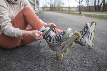Obraz premium Girl sitting on the road and tying the laces on roller skates, close-up. Concept: sports, healthy lifestyle.