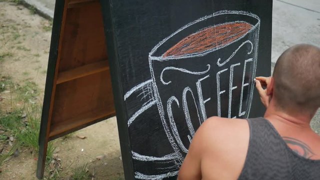 Young Man Draws Art on Chalkboard Advertising Pillar near Coffee Shop. HD Slowmotion Closeup Footage.