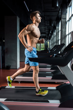 Young adult man running on treadmill in gym