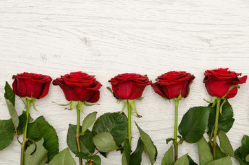 Fototapeta na wymiar Five red rose on a light wooden background at the edge of the frame, top view. Space for text