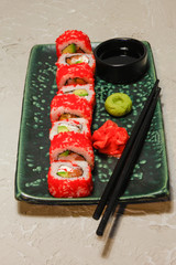 Roll on green plate with ginger, wasabi and soy sauce on creme background