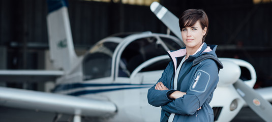 Smiling female pilot posing with her plane - obrazy, fototapety, plakaty