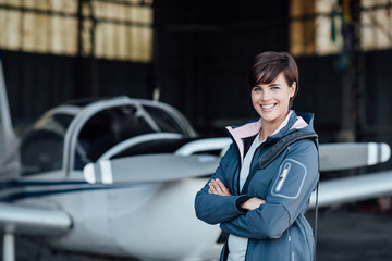 Smiling female pilot posing with her plane - obrazy, fototapety, plakaty