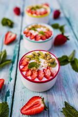 Tasty breakfast yogurt with fresh strawberries and fruits on wooden background.