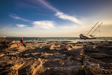 A man look the shipwrecked Boat in Calasetta, on the coast of south Sardinia where is sitting even...