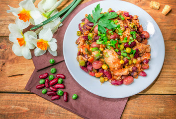 Homemade Stewed beans with chicken meat green peas and vegetables served with cut green onion and parsley on a white plate and croutons on wooden table