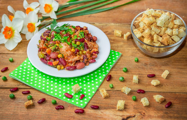Homemade Stewed beans with chicken meat green peas and vegetables served with cut green onion and parsley on a white plate and croutons on wooden table