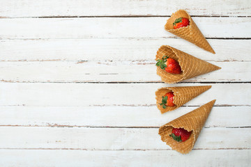 fresh red strawberries in waffle cones on white wooden tabletop, berries on wood concept