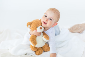 Portrait of adorable small baby boy with teddy bear playing on bed, 1 year old baby concept