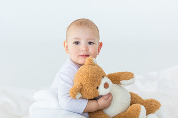 Portrait of adorable small baby boy with teddy bear playing on bed, 1 year old baby concept