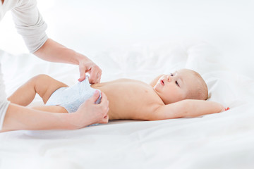 Cropped shot of mother changing diaper of adorable baby boy lying on bed, 1 year old baby concept