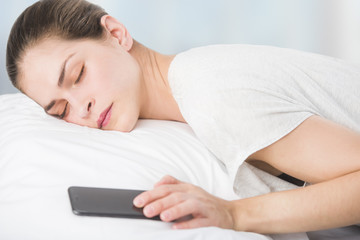 a beautiful young woman in bed, is pressing the snooze button in her phone