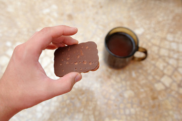 Hand holds a cookie, against a background of a cup of tea