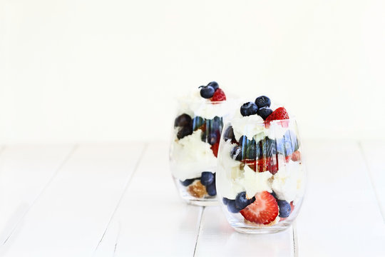 Trifle made with blueberries, strawberries, whipped cream and star shaped pound cake against a white wood background. Perfect for fourth of July. Shallow depth of field with selective focus.