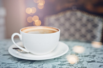 Cup of cappuccino on the table with lace tablecloth. Intentional sun glare