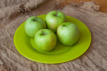 A plate with green apples on the sackcloth texture background
