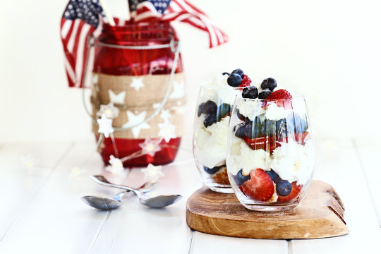 Trifle made with blueberries, strawberries, whipped cream and star shaped pound cake with American flags in background. Shallow depth of field with selective focus.