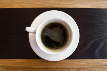 A cup of black coffee in a white cup on wooden background. 