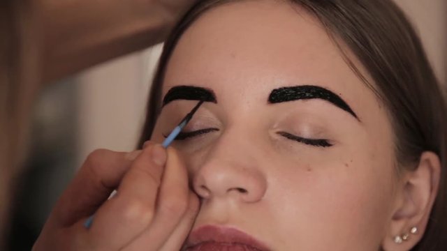 Professional make-up artist drawing eyebrows of client with henna