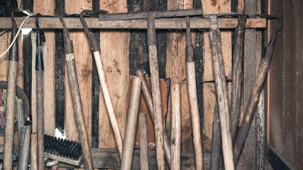 old rustic tools, hanging on the wooden wall of a house.