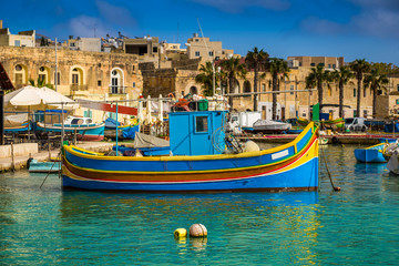 Marsaxlokk, Malta - Traditional colorful maltese Luzzu fisherboat at the old village of Marsaxlokk with turquoise sea water and palm trees on a summer day