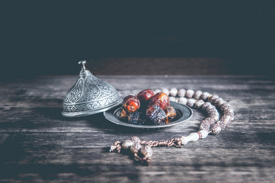 Date-palm is placed on silver. date palm fruits or kurma, ramadan on a wooden black background.