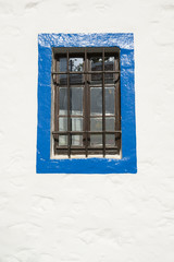 Fototapeta premium Simple window with iron bars surrounded by blue border on a white stucco wall