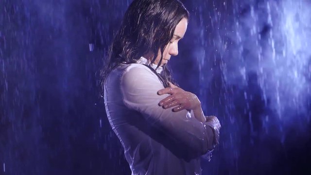 A woman stands in the pouring rain in the light of the moon