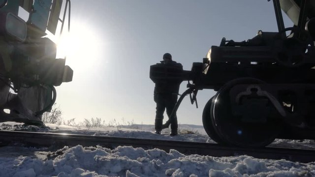 Handheld tracking shot of coupling railway carriage for linking freight train wagon with diesel locomotive at dusk in winter period. Railman silhouette watching the process.