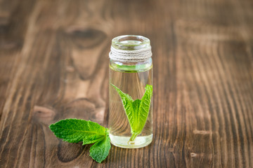 Mint essential oil in glass bottle on wooden background