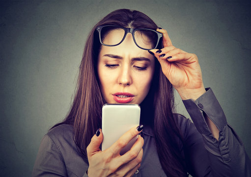 Woman with glasses having trouble seeing cell phone has vision problems.