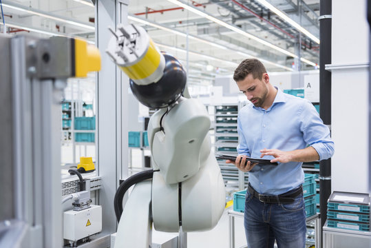 Man using tablet next to assembly robot in factory shop floor