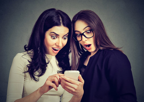 Two amazed women roommates watching offers on line on a smart phone.