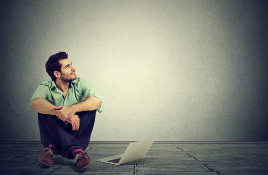 man with laptop computer sitting on a floor planning daydreaming