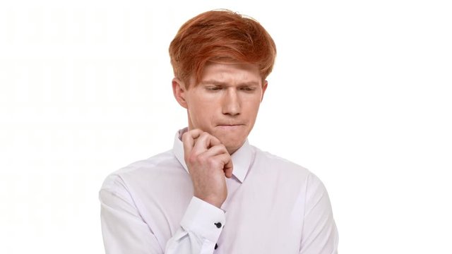Thoughtfull Caucasian young boy with ginger hair standing on white background and holding his chin. Then taking deep breath